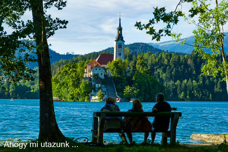 Szlovénia látnivalók - a bledi tó, előtérben egy pad, ahol idősek ebszélgetnek a tó felé fordulva.